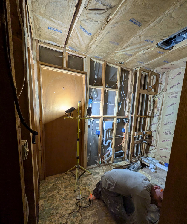 Worker insulating unfinished room with exposed wall studs and ceiling