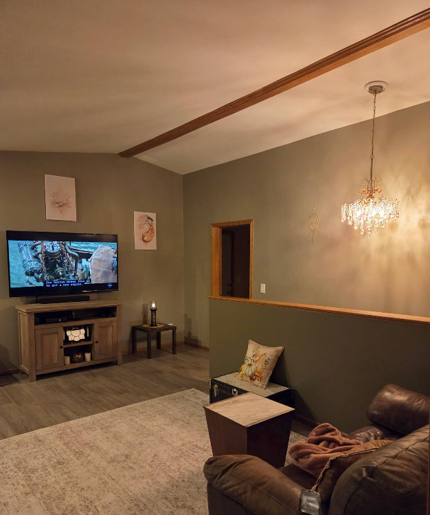 Living room with TV, chandelier, gray walls, sofa, and rug