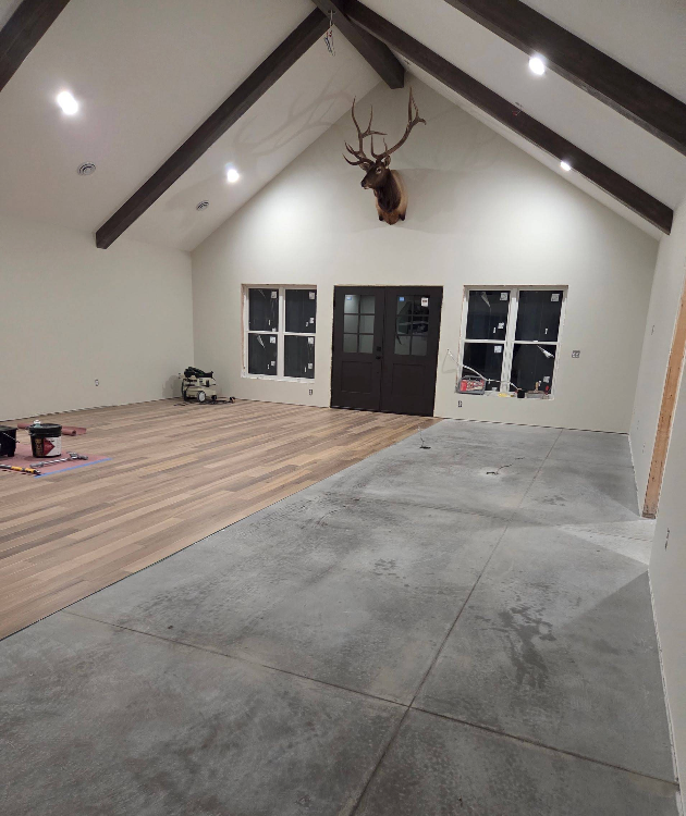 Empty room with vaulted ceiling, deer head mount, wood floor on left, and large concrete slab on right
