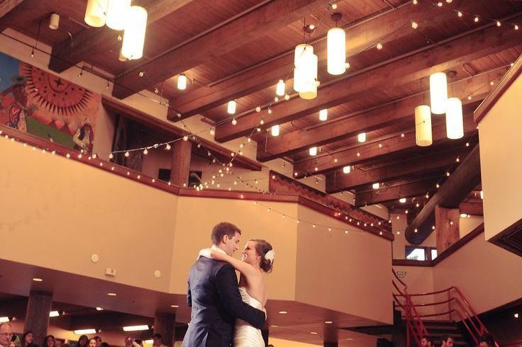 A bride and groom are dancing in a large room with lights hanging from the ceiling.