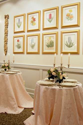 A table with plates and candles on it in front of a wall with pictures of flowers on it.