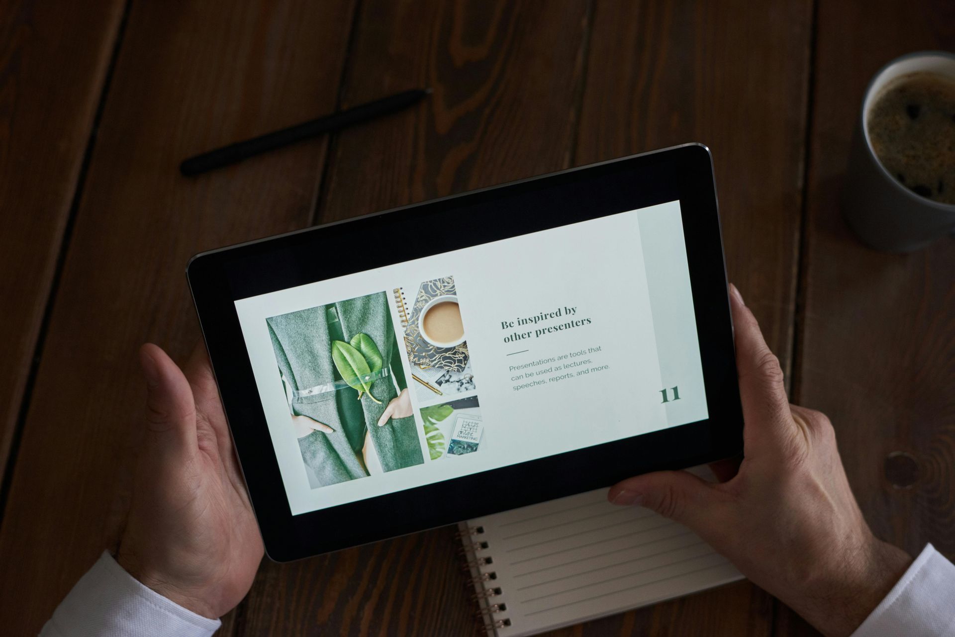 A person is holding a tablet in their hands on a wooden table.