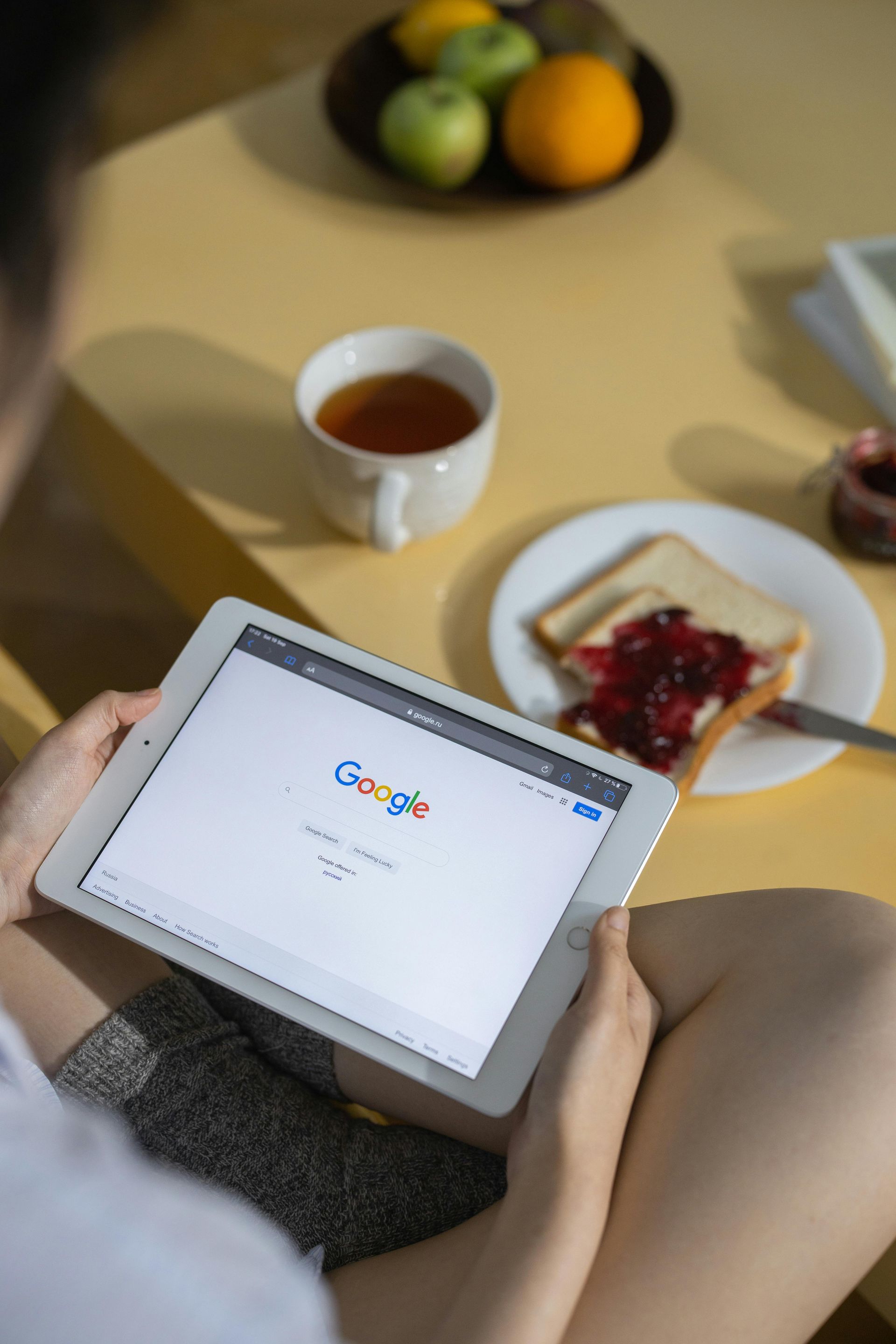 A woman is sitting at a table using a tablet to search for google.