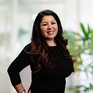 Woman in black top smiling, posed in front of blurred office background.