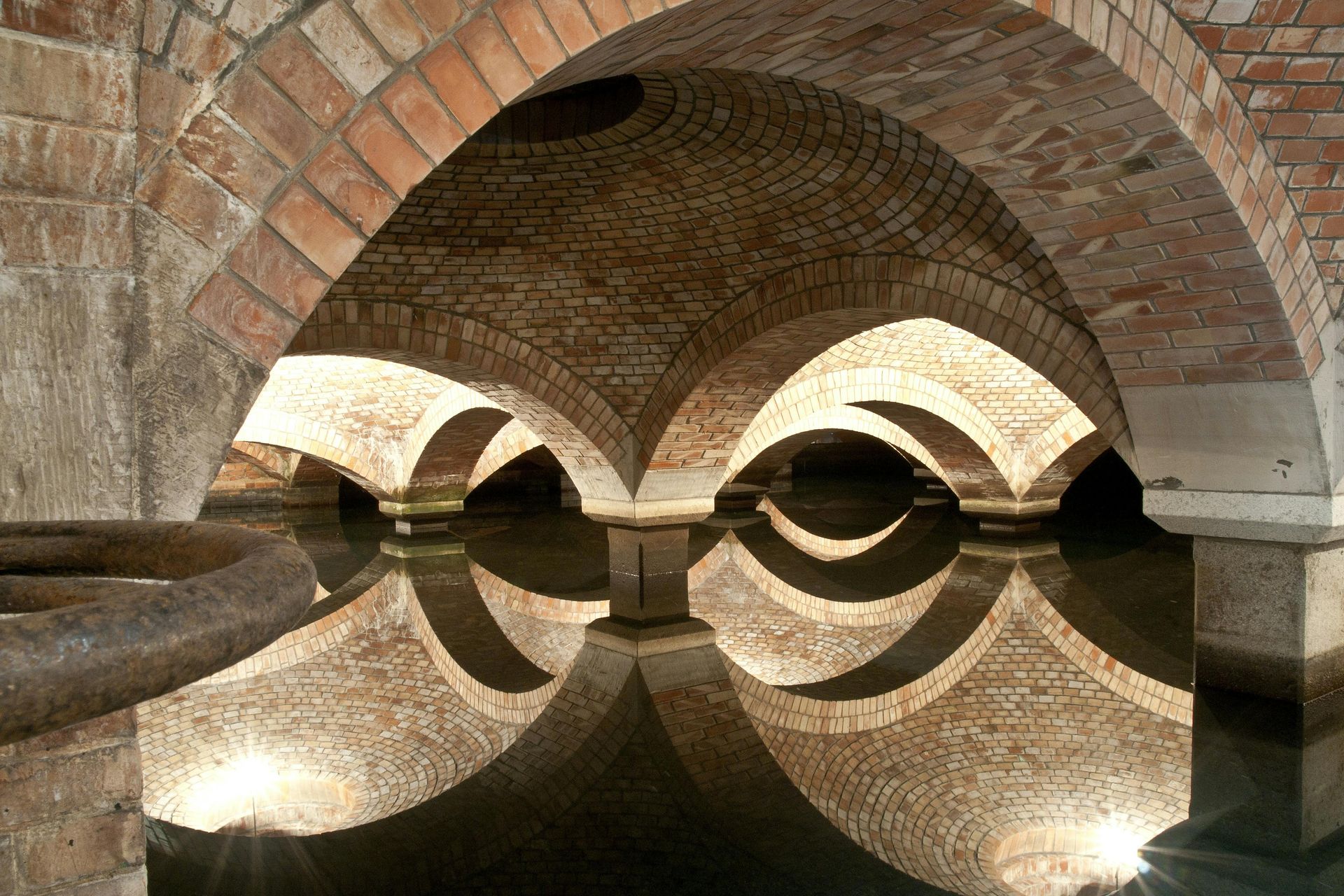Brick arched bridge arches reflected in calm water, creating symmetrical tunnel-like patterns