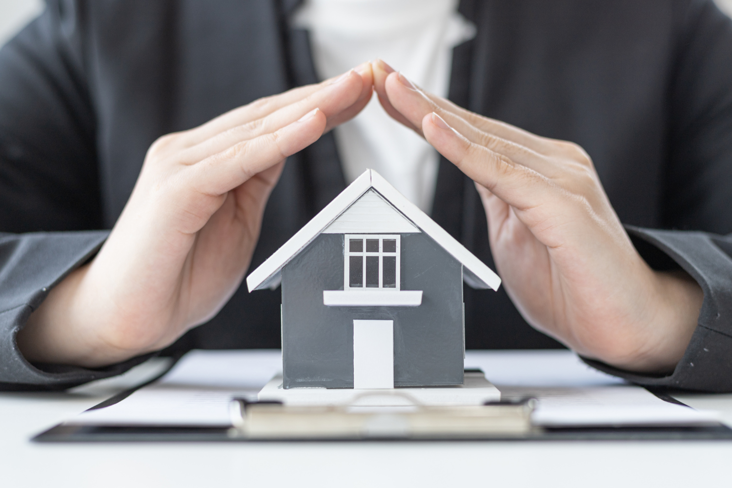 Hands protecting a model house; concept of home insurance or protection.