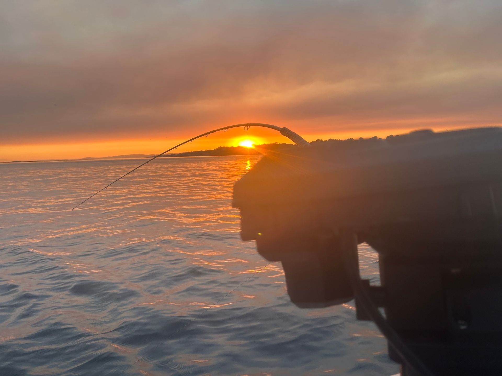 Fishing rod bent at sunset over snowy water.