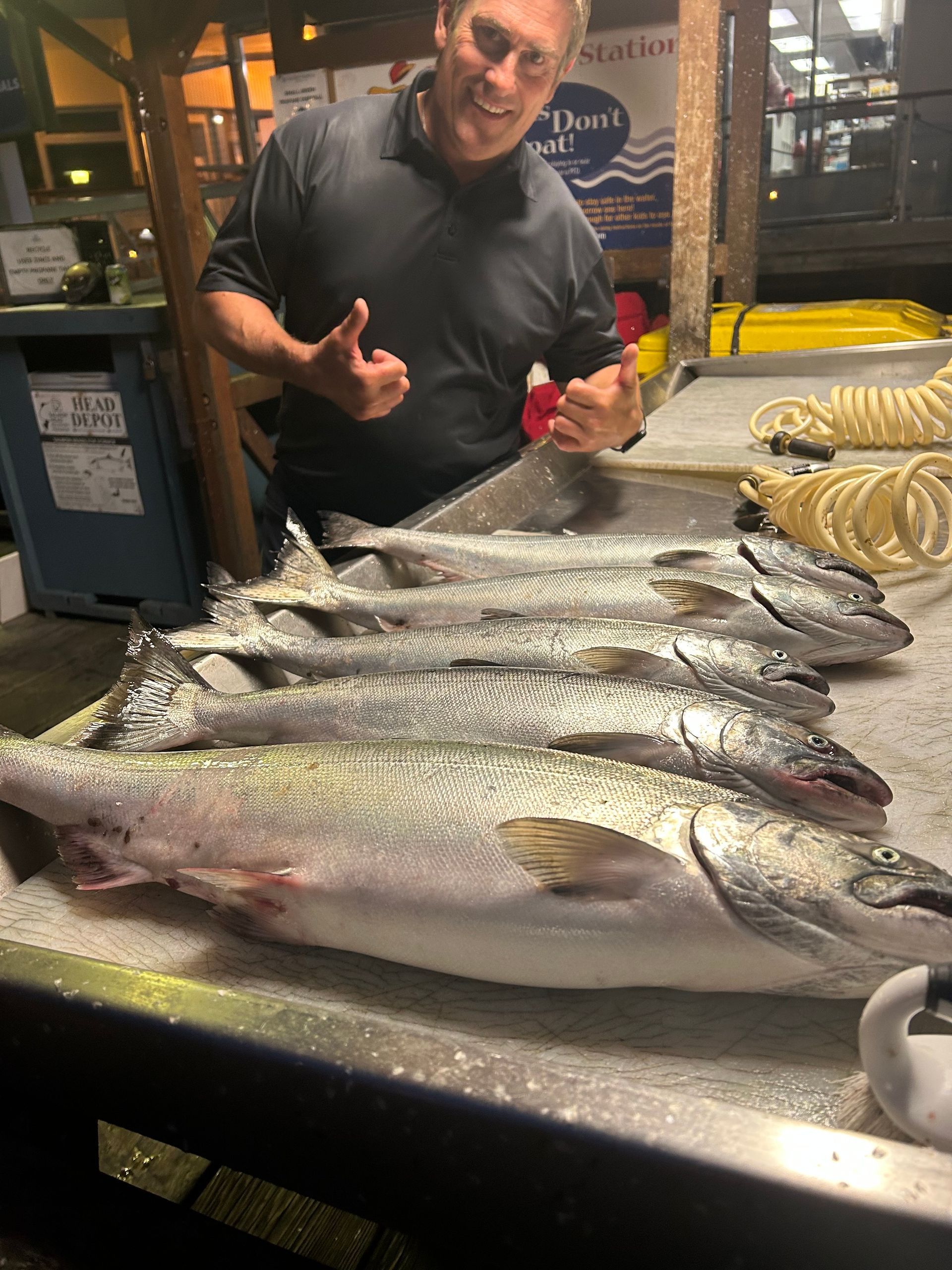 Man gives thumbs up next to large salmon on ice at a dock.