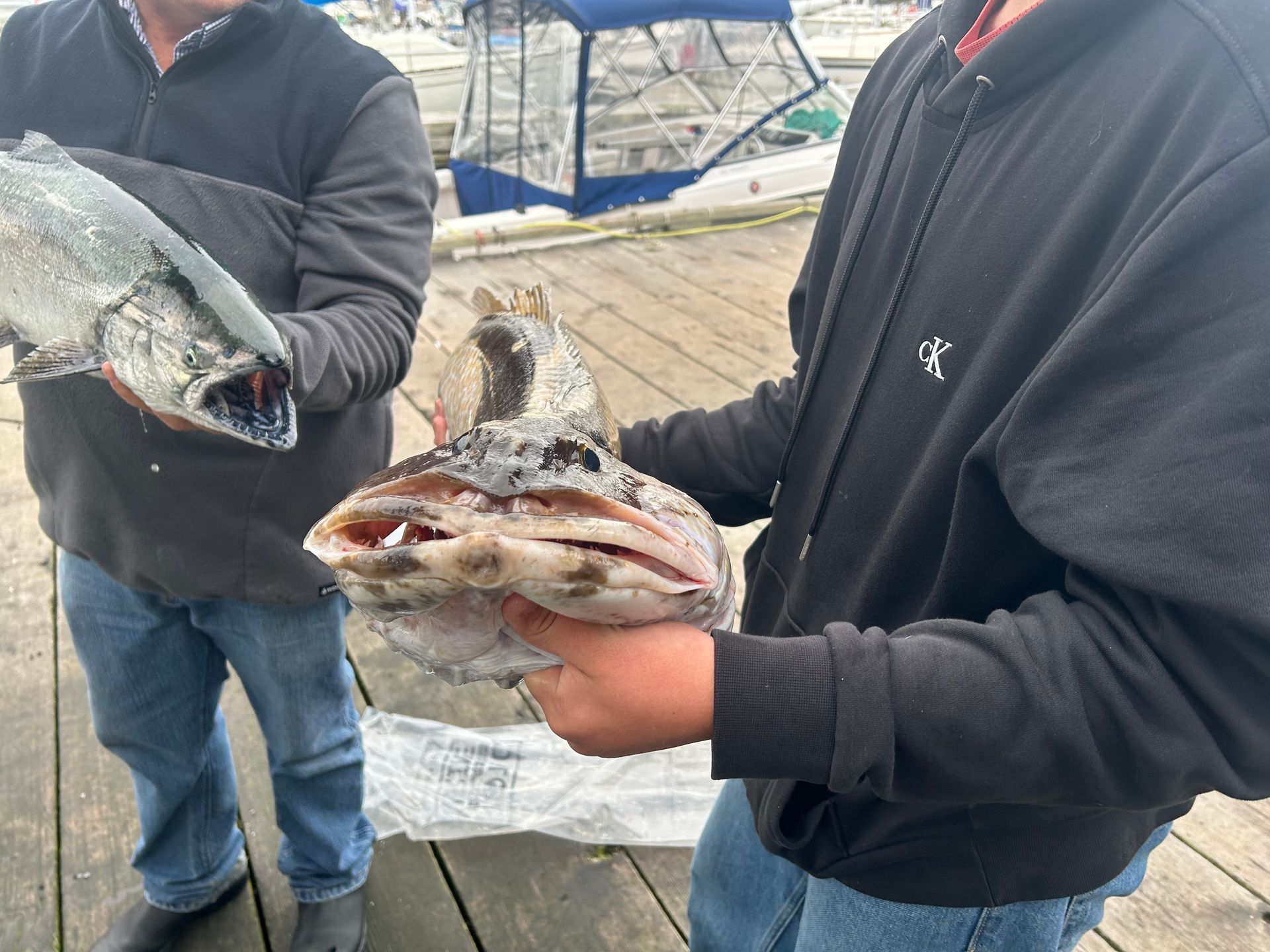 Two people holding freshly caught fish on a wooden dock.