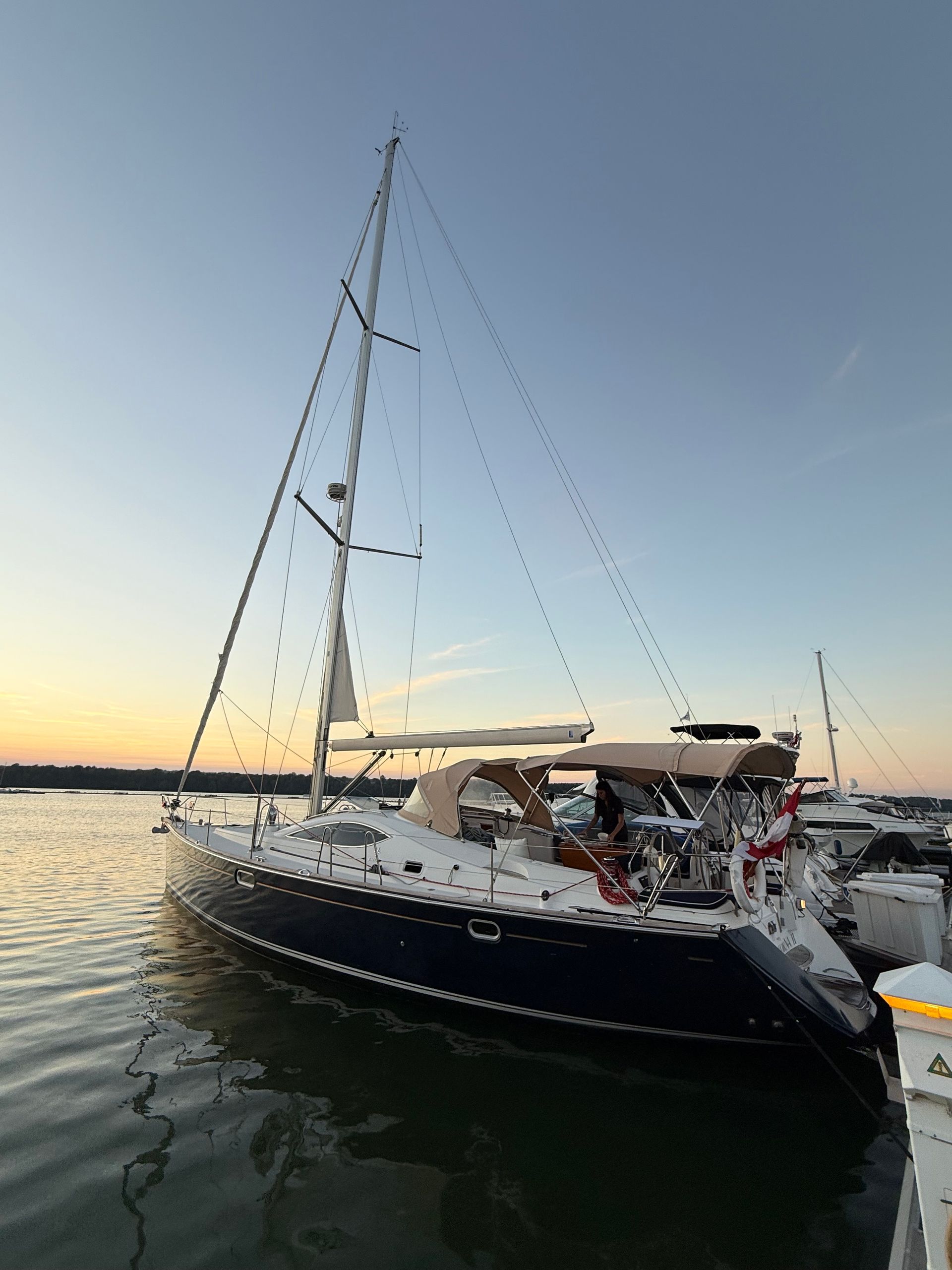 Sailboat docked at dusk with blue hull, white sails, and beige canopy.
