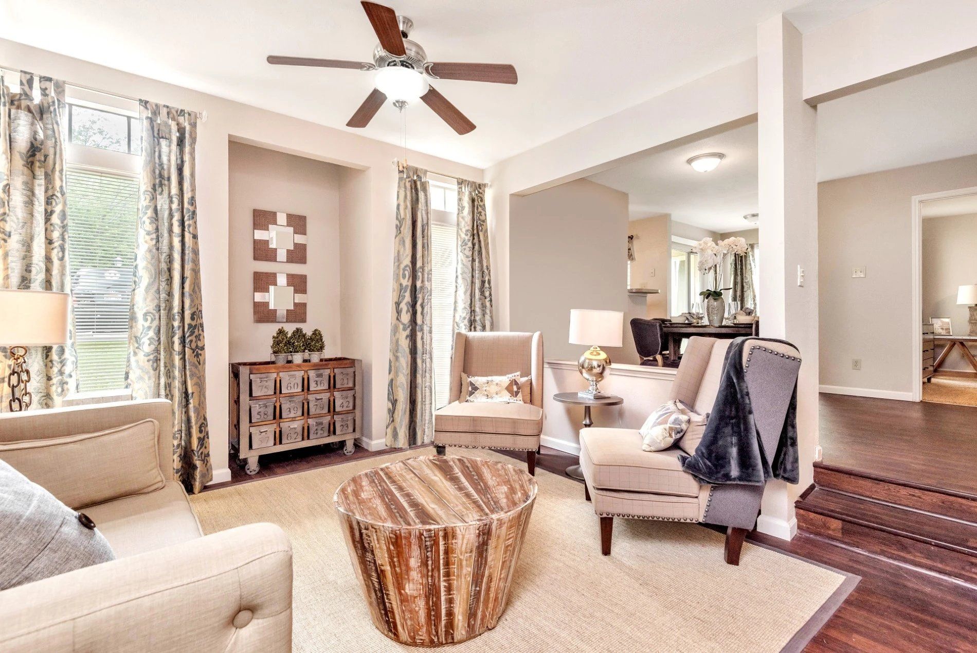 Bright living room with cream chairs, wood coffee table, patterned rug, and ceiling fan near a staircase at Steeplechase Apartments for Rent in Knoxville, TN