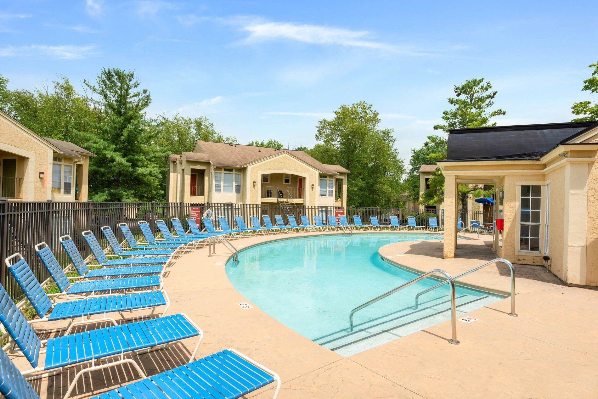 Outdoor resort pool with blue lounge chairs and beige cabanas under a bright sky at Steeplechase Apartments for Rent in Knoxville, TN