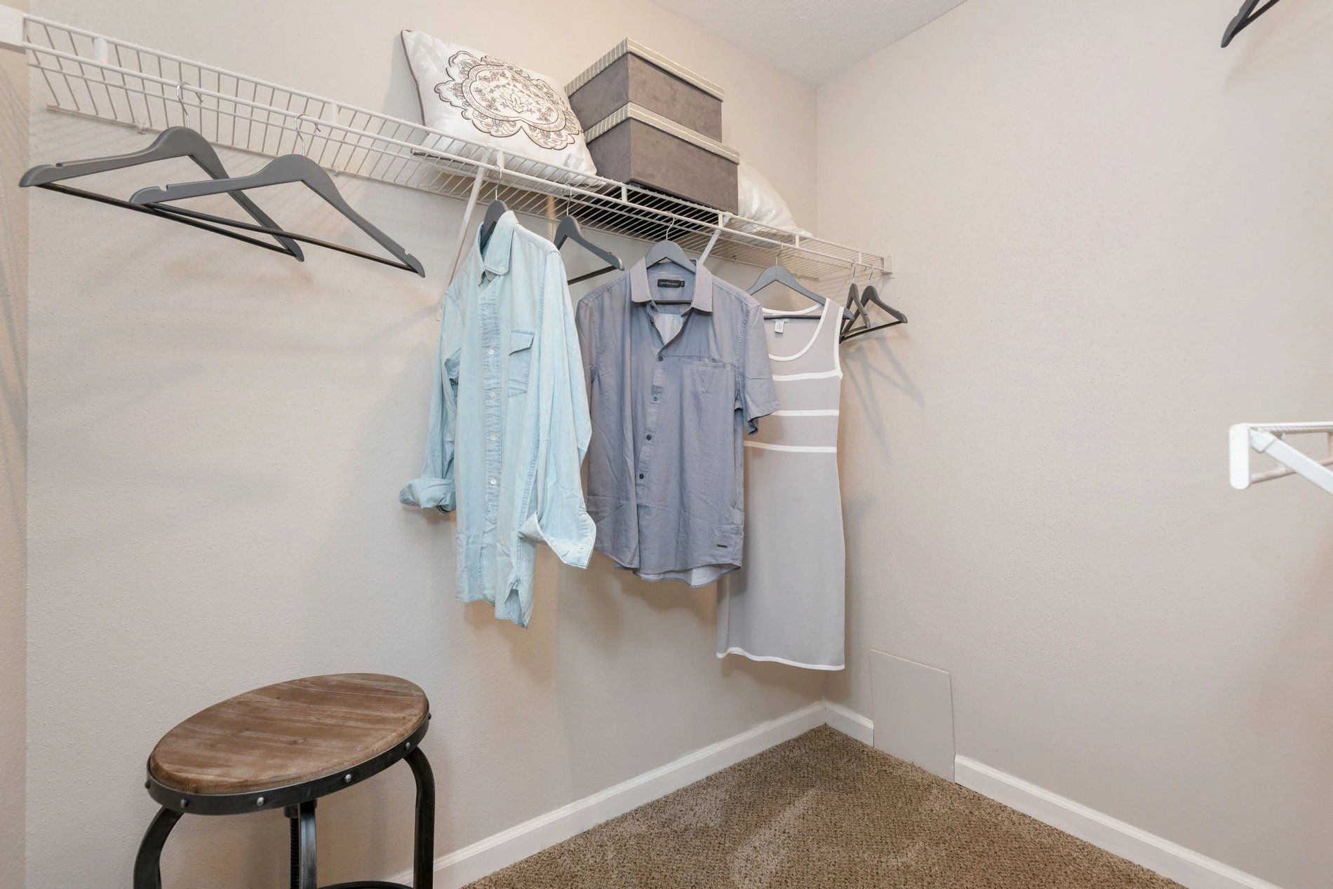 Small walk-in closet with hanging clothes, wire shelves, and a stool on carpet at Steeplechase Apartments for Rent in Knoxville, TN