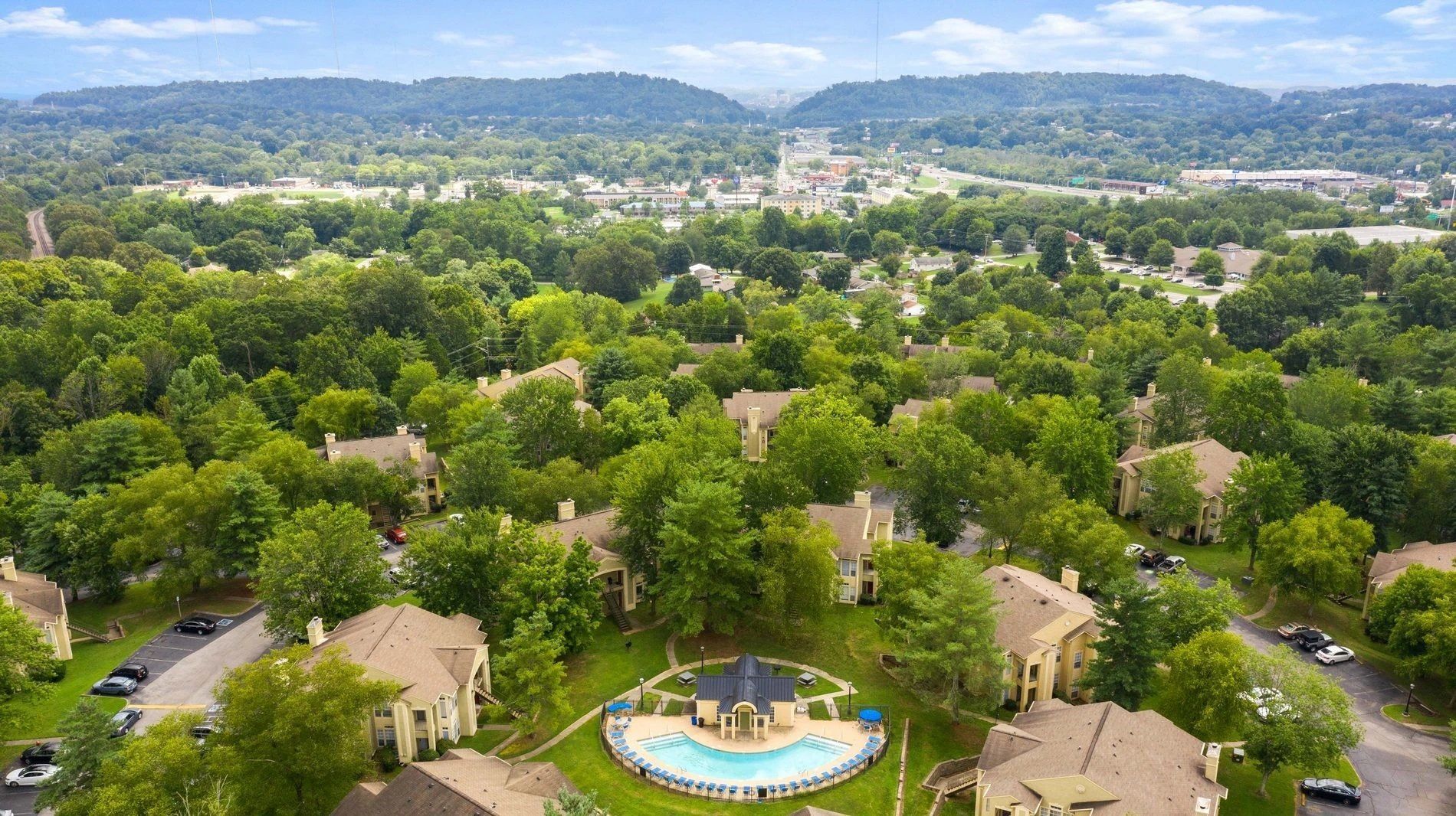 Aerial view of a green suburban neighborhood with a central fountain and distant hills beyond at Steeplechase Apartments for Rent in Knoxville, TN