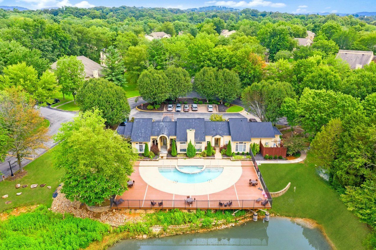 Aerial view of a lakeside home with a deck and swimming pool surrounded by lush green trees at Steeplechase Apartments for Rent in Knoxville, TN