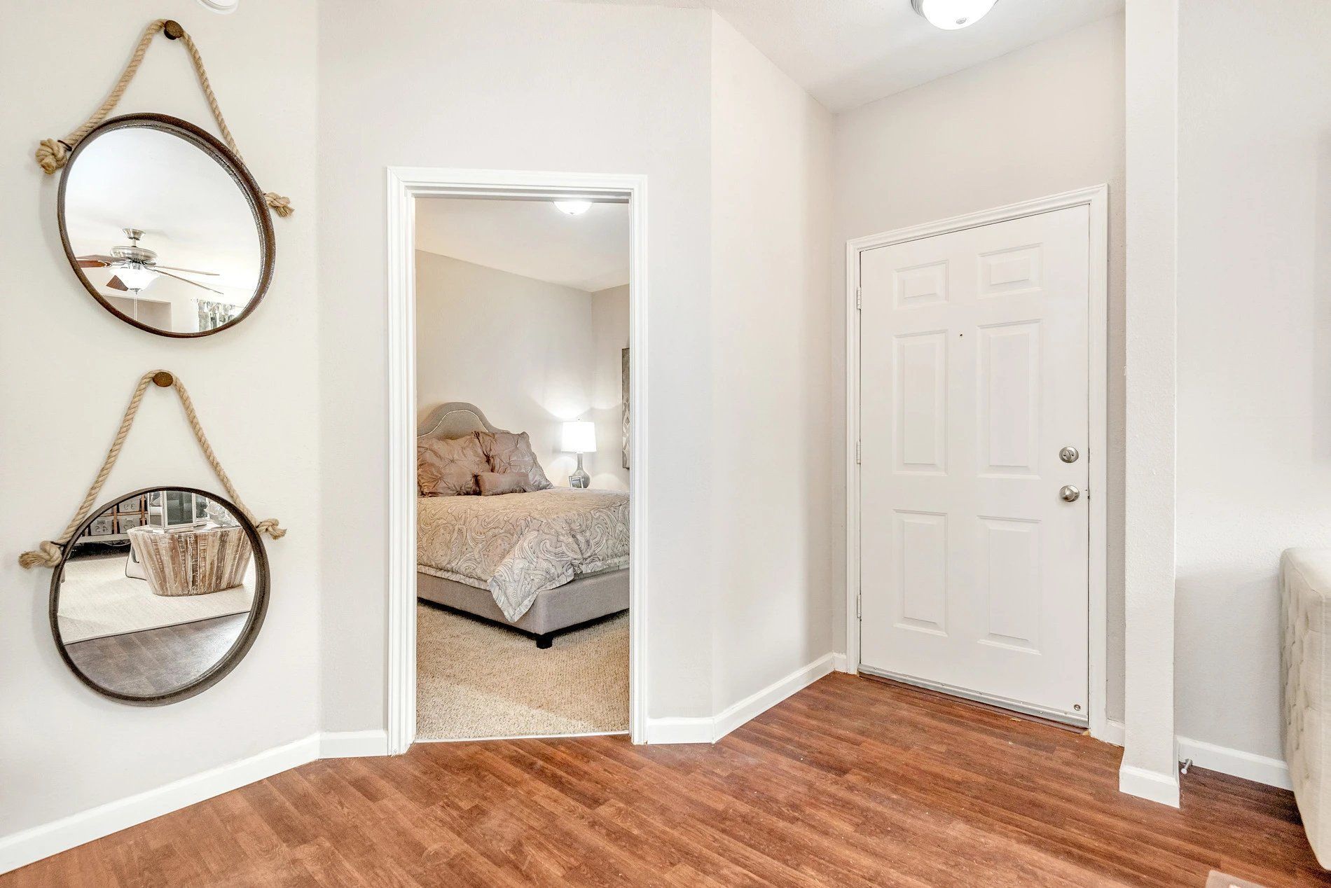Hallway with hardwood floor, mirrored wall decor, white doors, and a glimpse into a carpeted bedroom at Steeplechase Apartments for Rent in Knoxville, TN