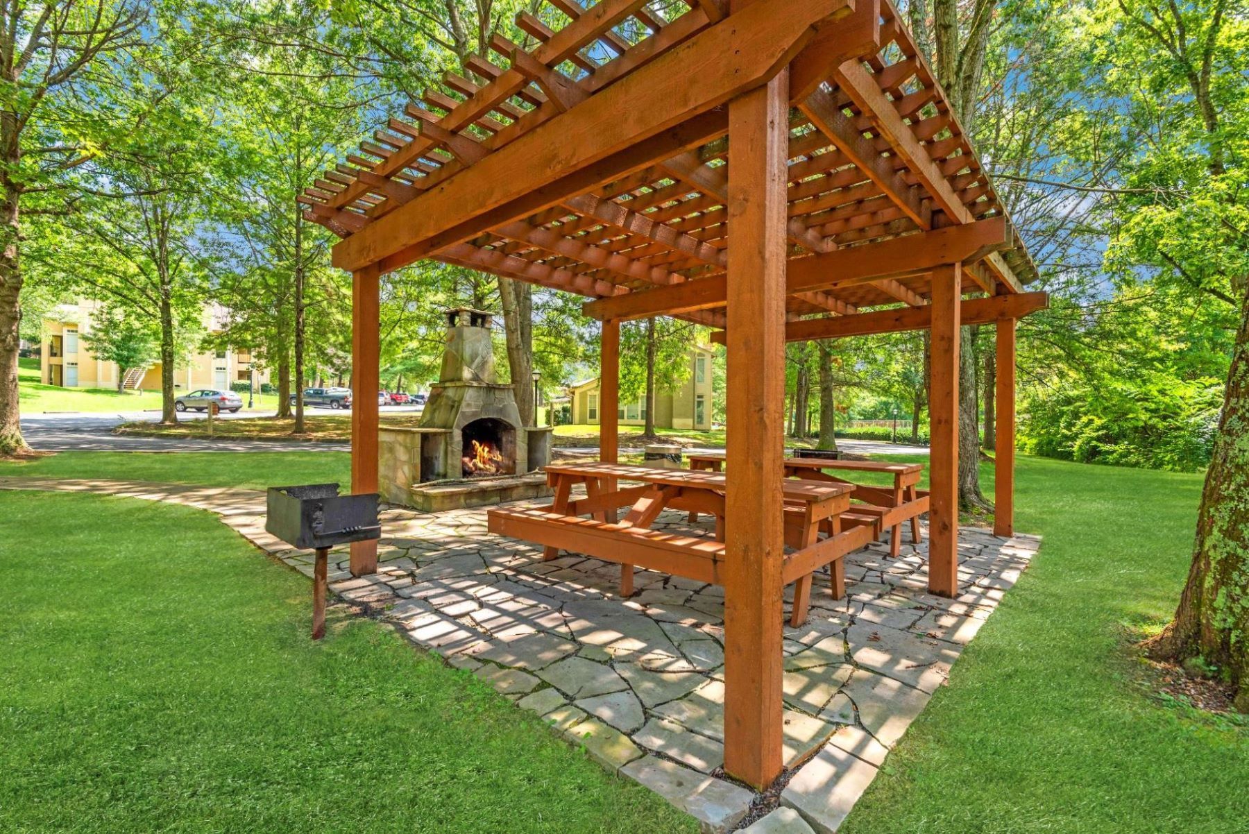 Wooden picnic shelter with built-in tables in a sunny park, surrounded by green trees and grass at Steeplechase Apartments for Rent in Knoxville, TN