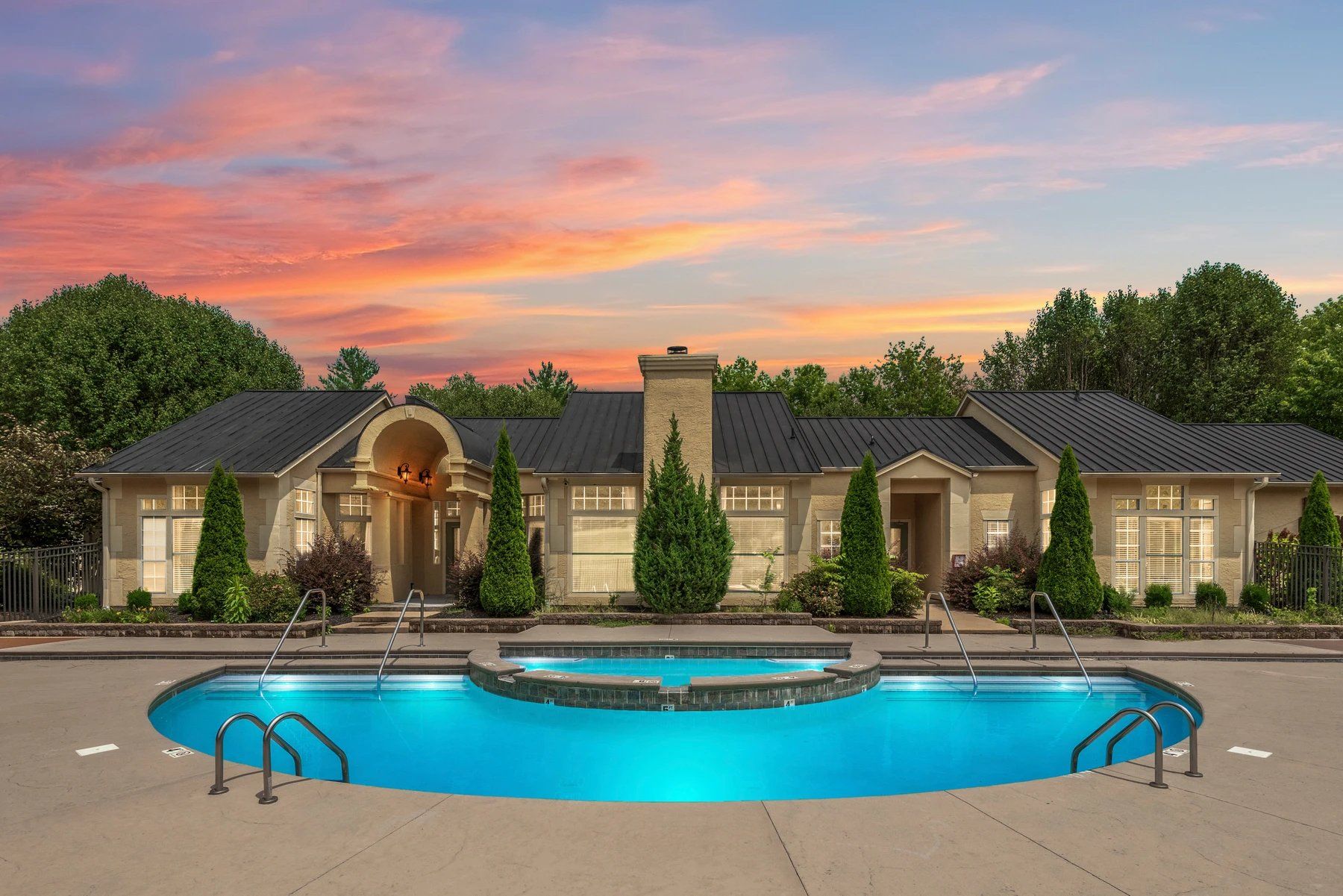 Luxurious home with a glowing blue pool at sunset, framed by trees and a pink-orange sky at Steeplechase Apartments for Rent in Knoxville, TN