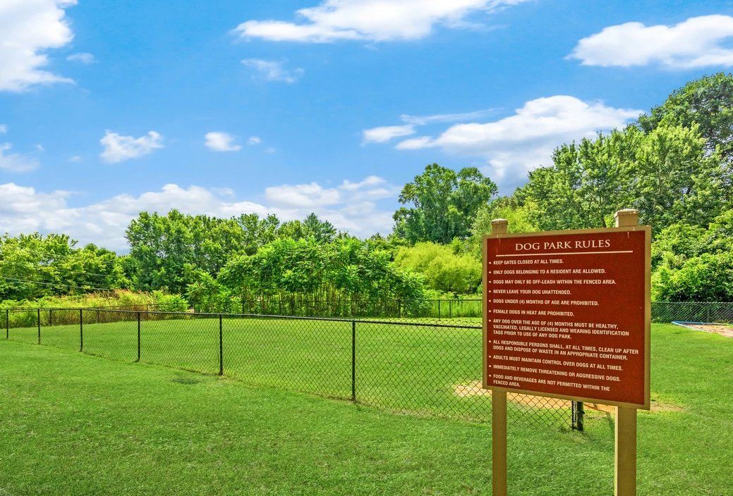 Fenced grassy field with trees and a brown information sign under a blue sky at Steeplechase Apartments for Rent in Knoxville, TN