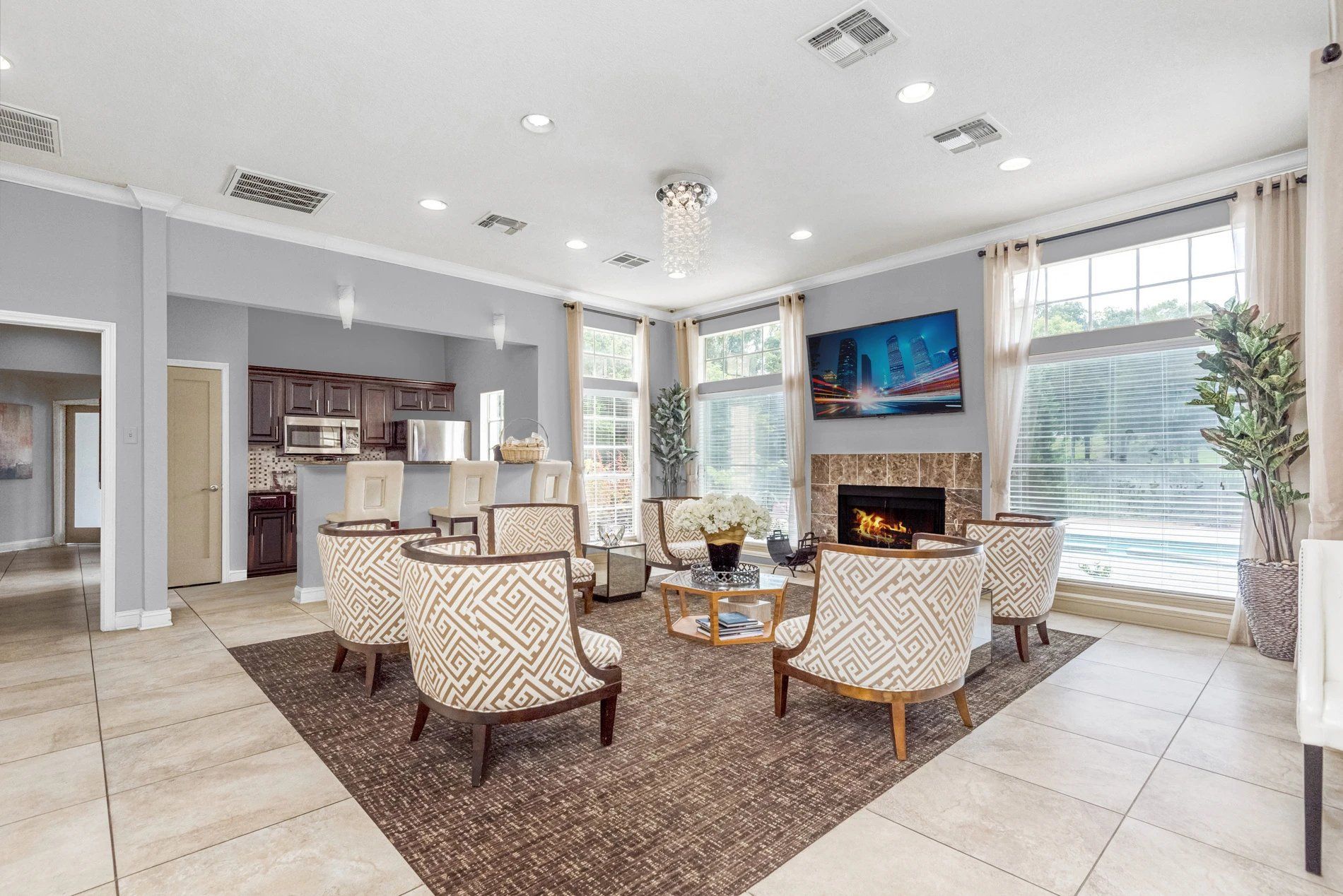 Bright modern living room with fireplace, TV, four chairs, and open kitchen by large windows at Steeplechase Apartments for Rent in Knoxville, TN