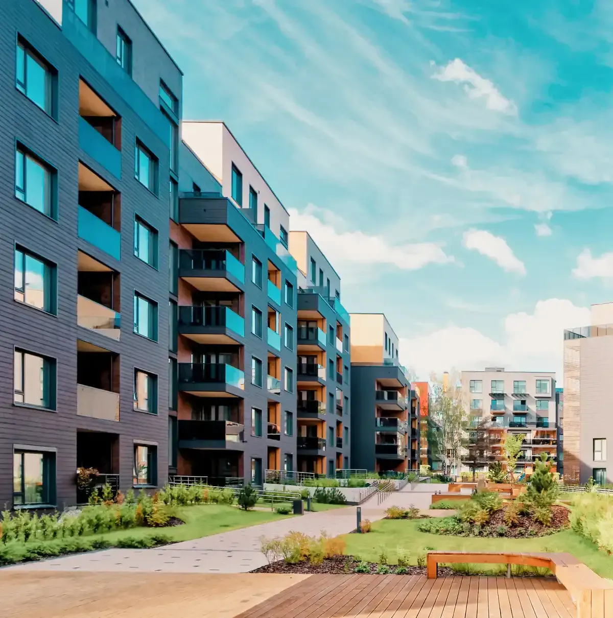 Modern apartment buildings with landscaped courtyard and walking paths under a blue sky