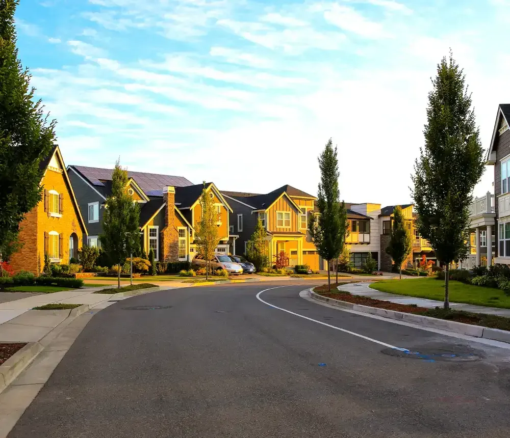 Curved street in a quiet suburban neighborhood with modern yellow houses and trees under a blue sky