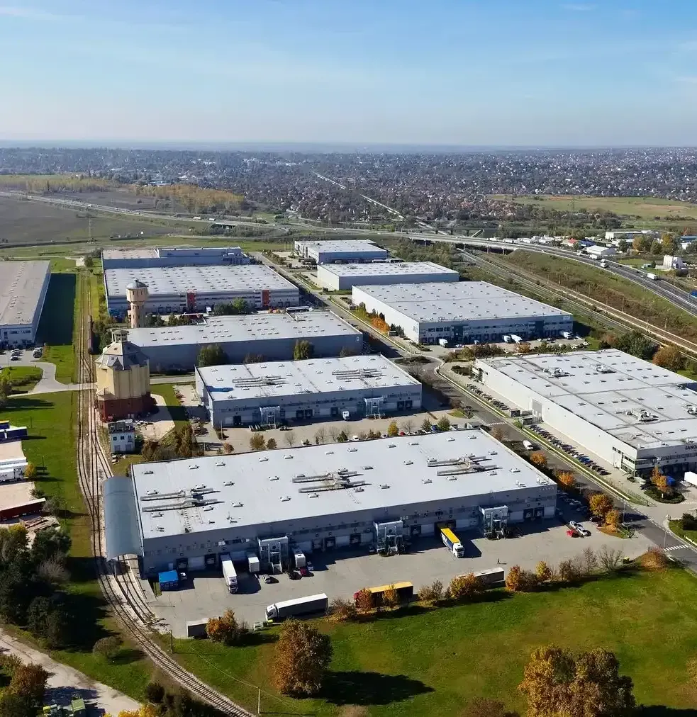 Aerial view of large industrial warehouse complex with trucks and parking lots on a clear day