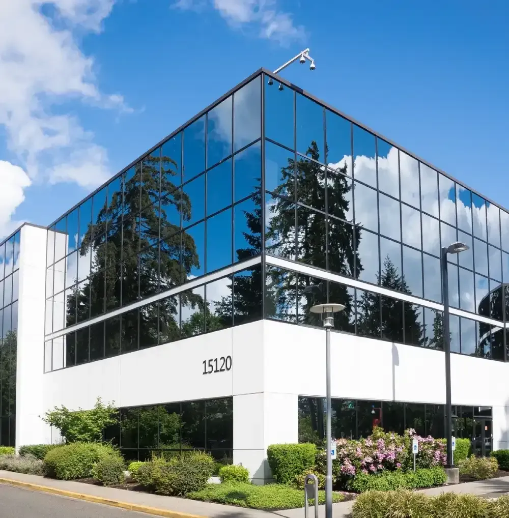 Modern office building with reflective glass windows and white exterior, surrounded by landscaping