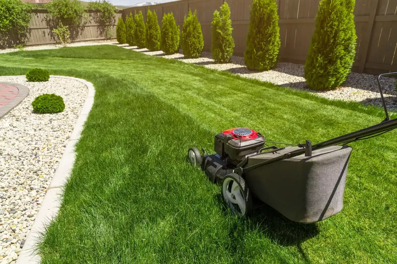 Lawn mower on a neatly trimmed green lawn beside a stone path and fence.