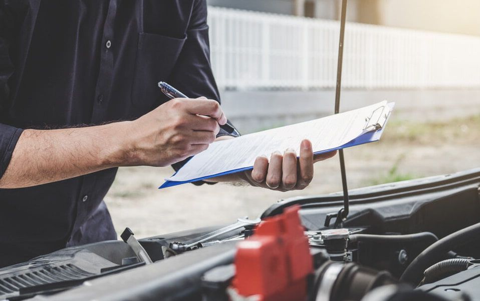 A Man Is Writing On A Clipboard While Standing Next To A Car — Goulburn Automotive Centre In Goulburn, NSW