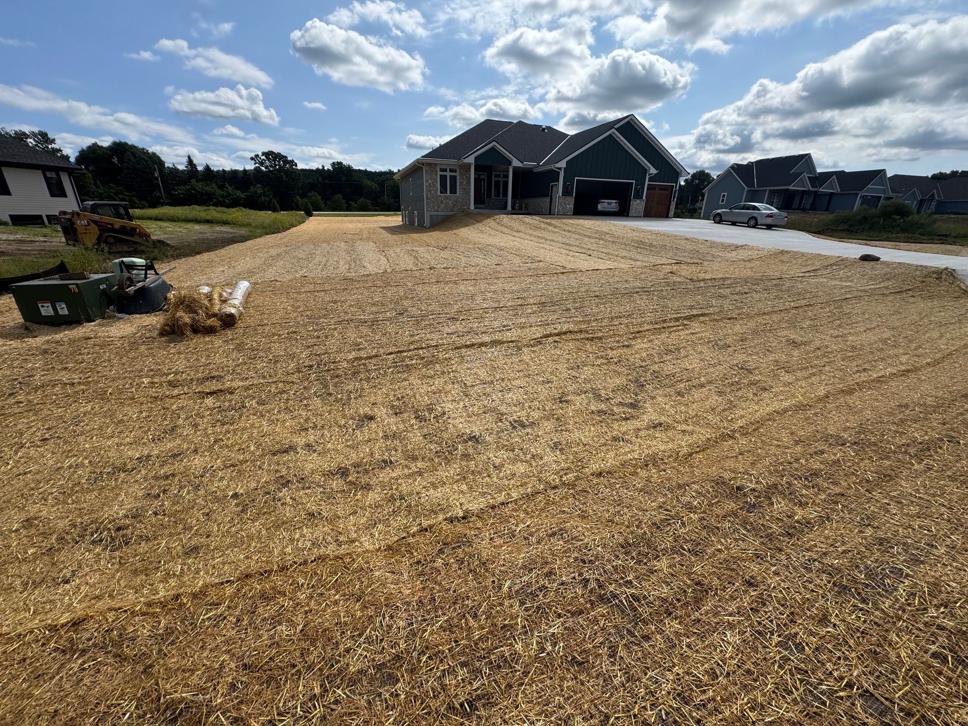 Newly landscaped yard covered in wood chips, with a house and blue sky in the background.
