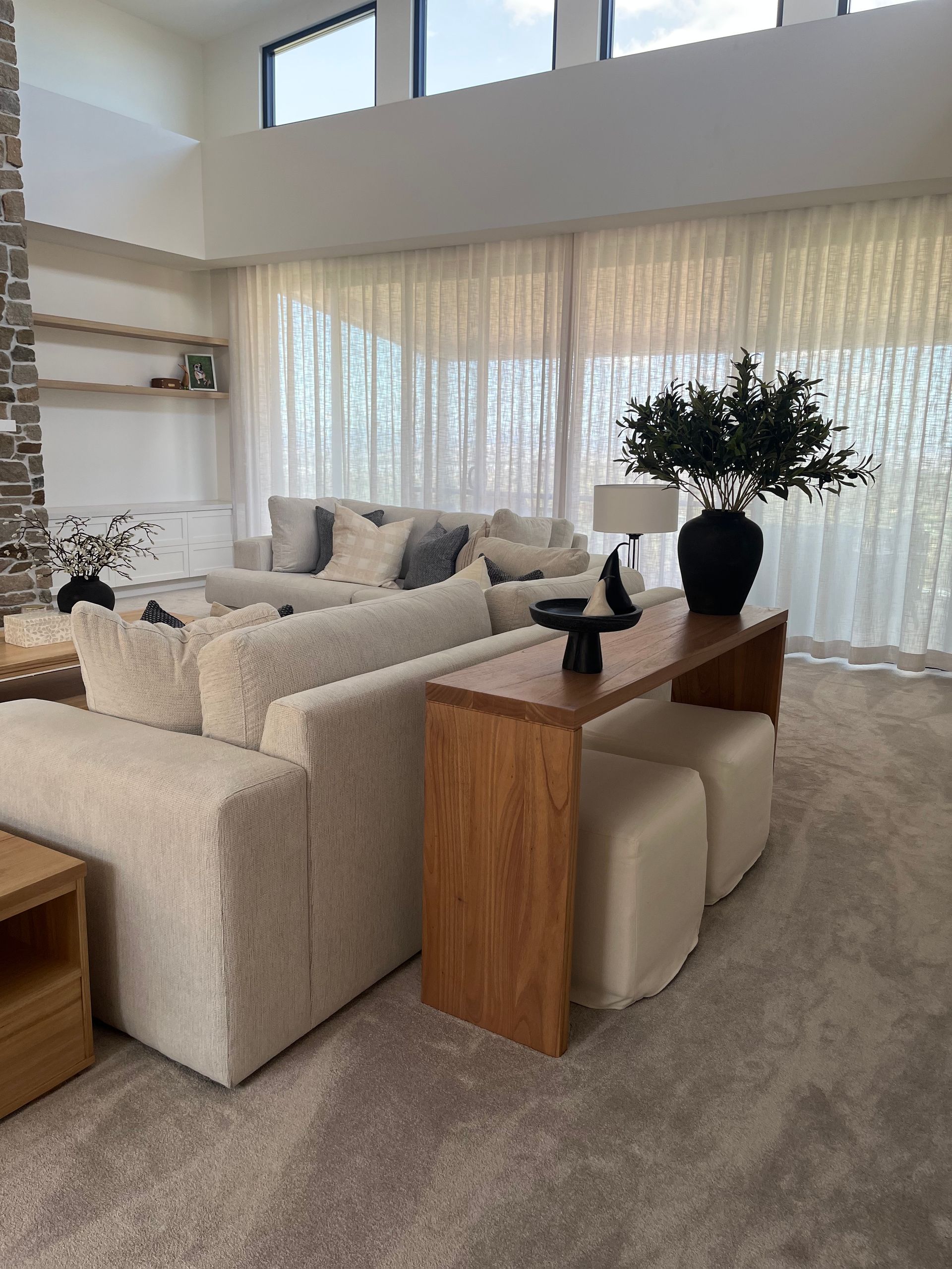 Bright modern living room with cream sofas, wooden console, and large window draped with sheer curtains