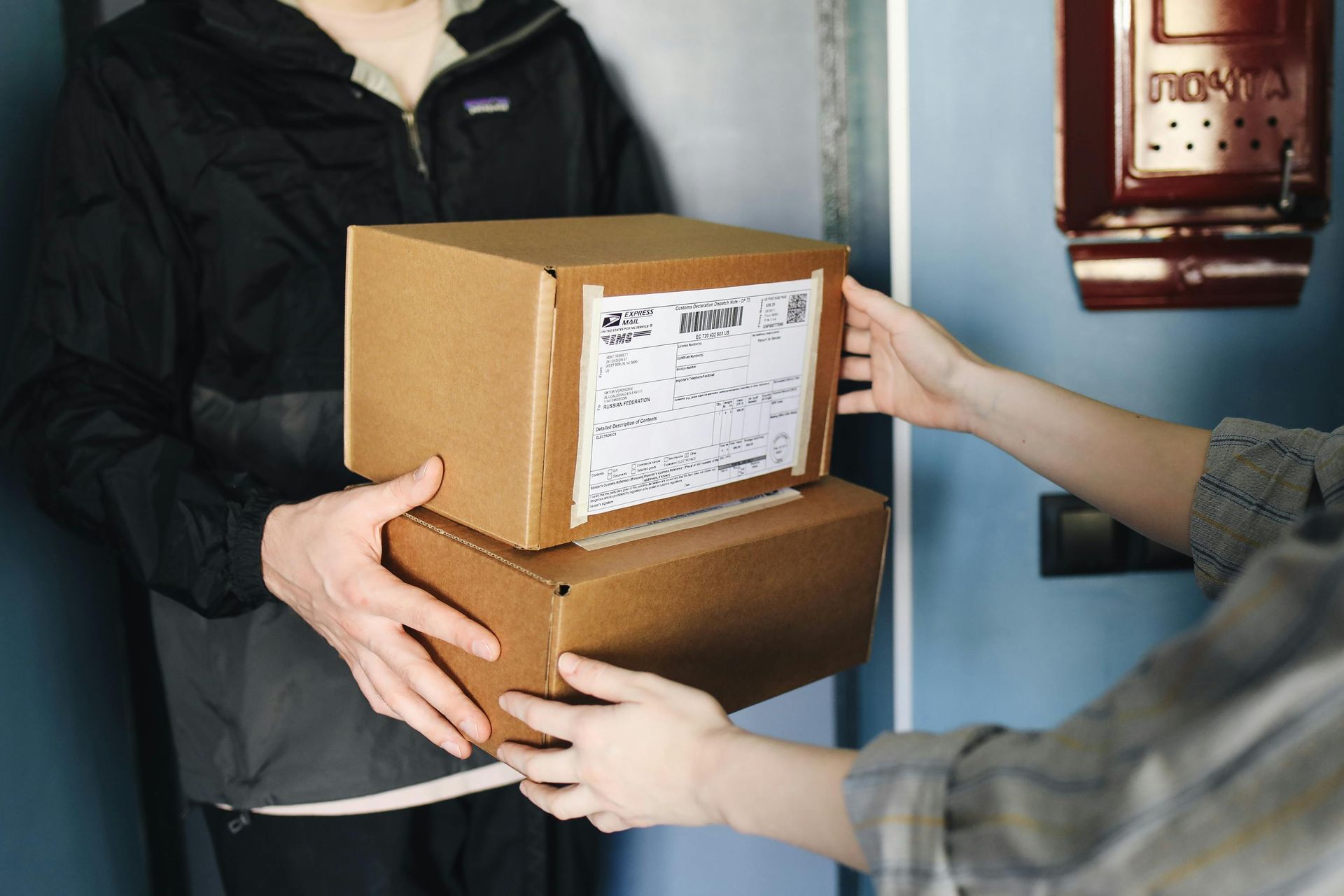Delivery person handing two stacked cardboard boxes to someone at a door.