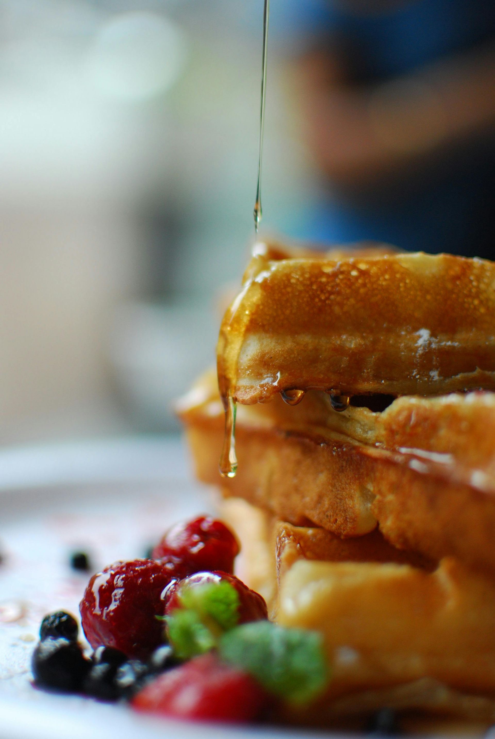 Syrup is being poured on a stack of waffles