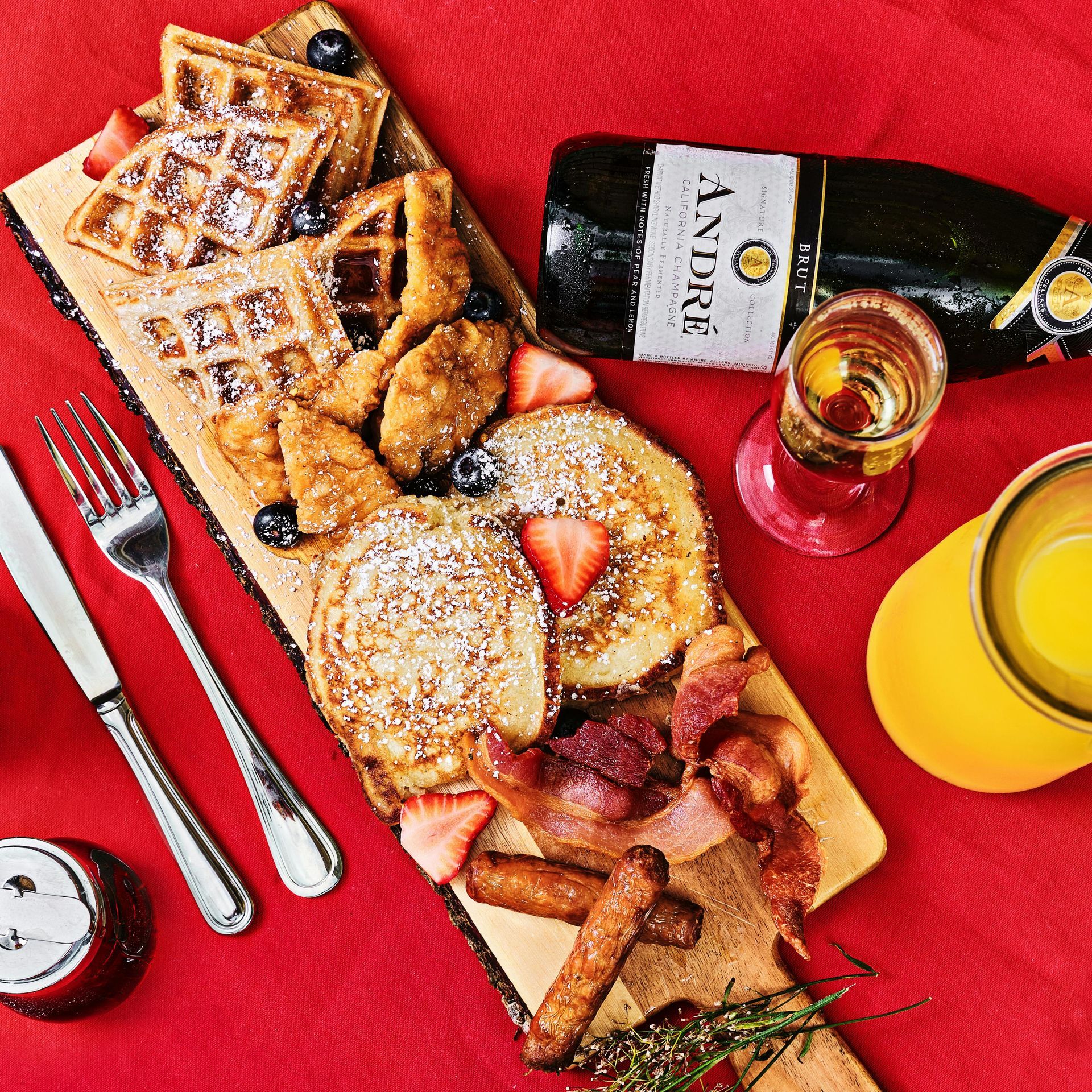 A wooden cutting board filled with food and a bottle of andre