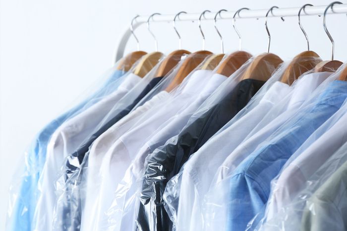 a row of shirts wrapped in plastic are hanging on a rack .