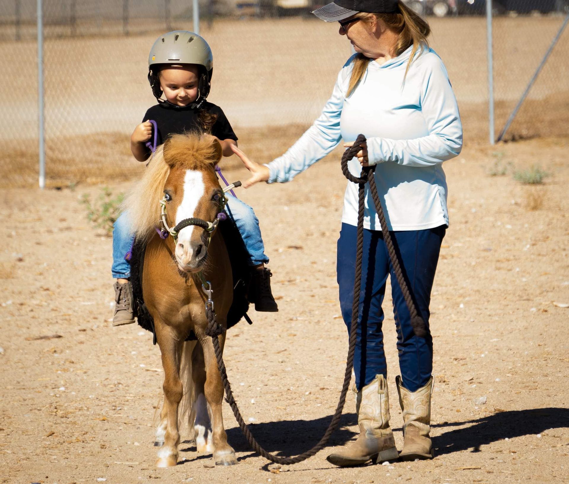 A little boy is riding a pony with a woman holding the reins