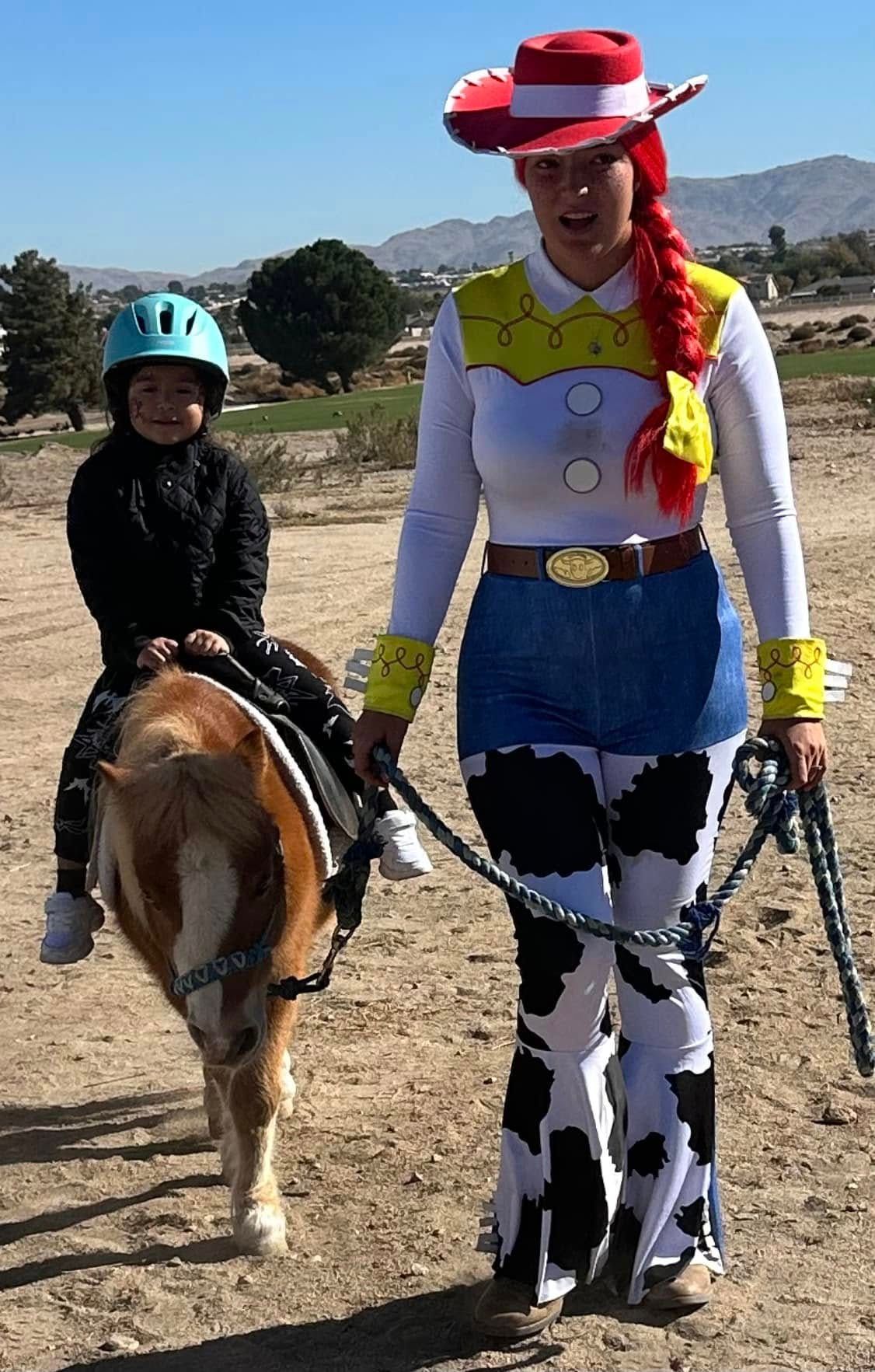 A woman in a jessie costume leads a child on a pony