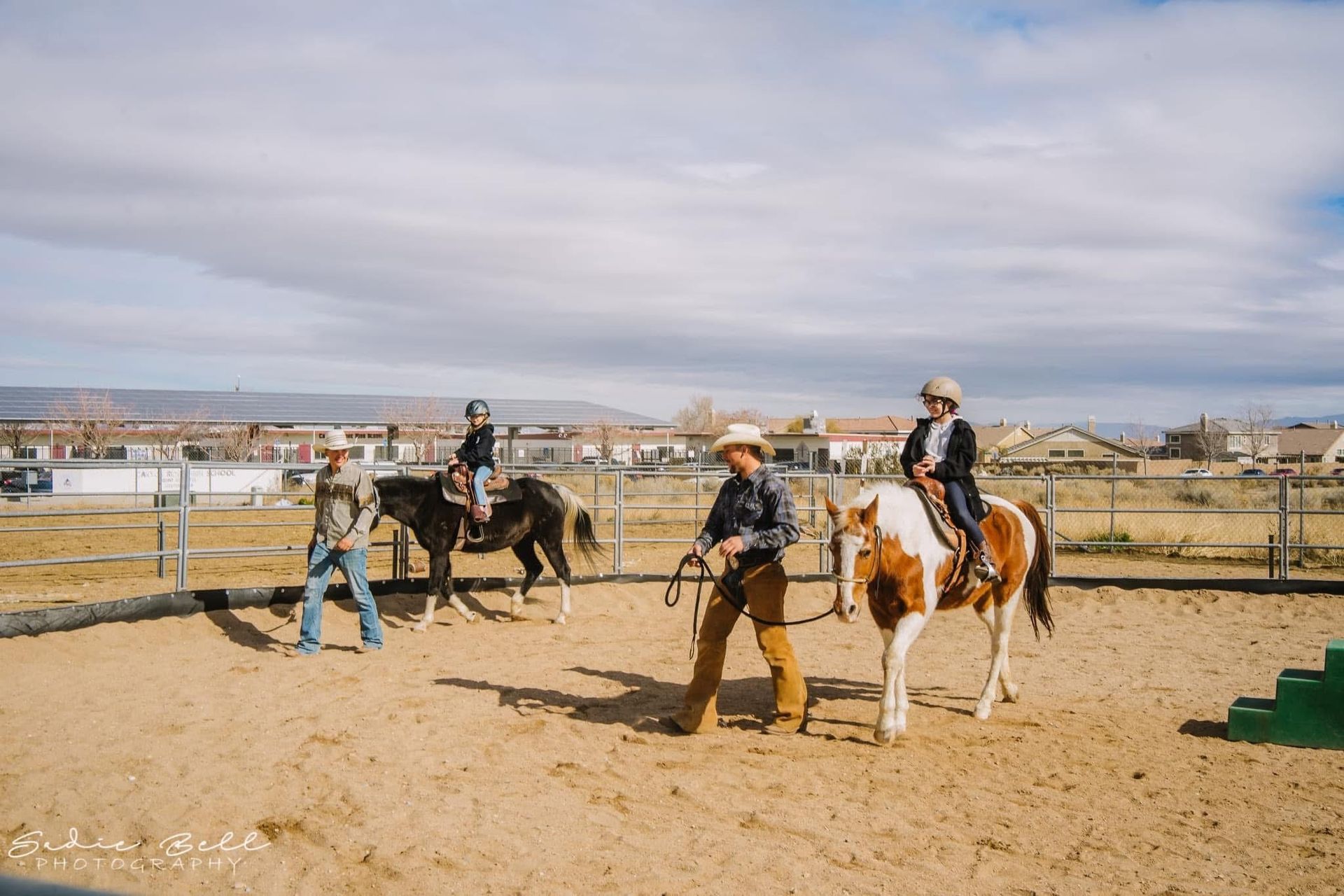 Two people are riding horses down a dirt road.