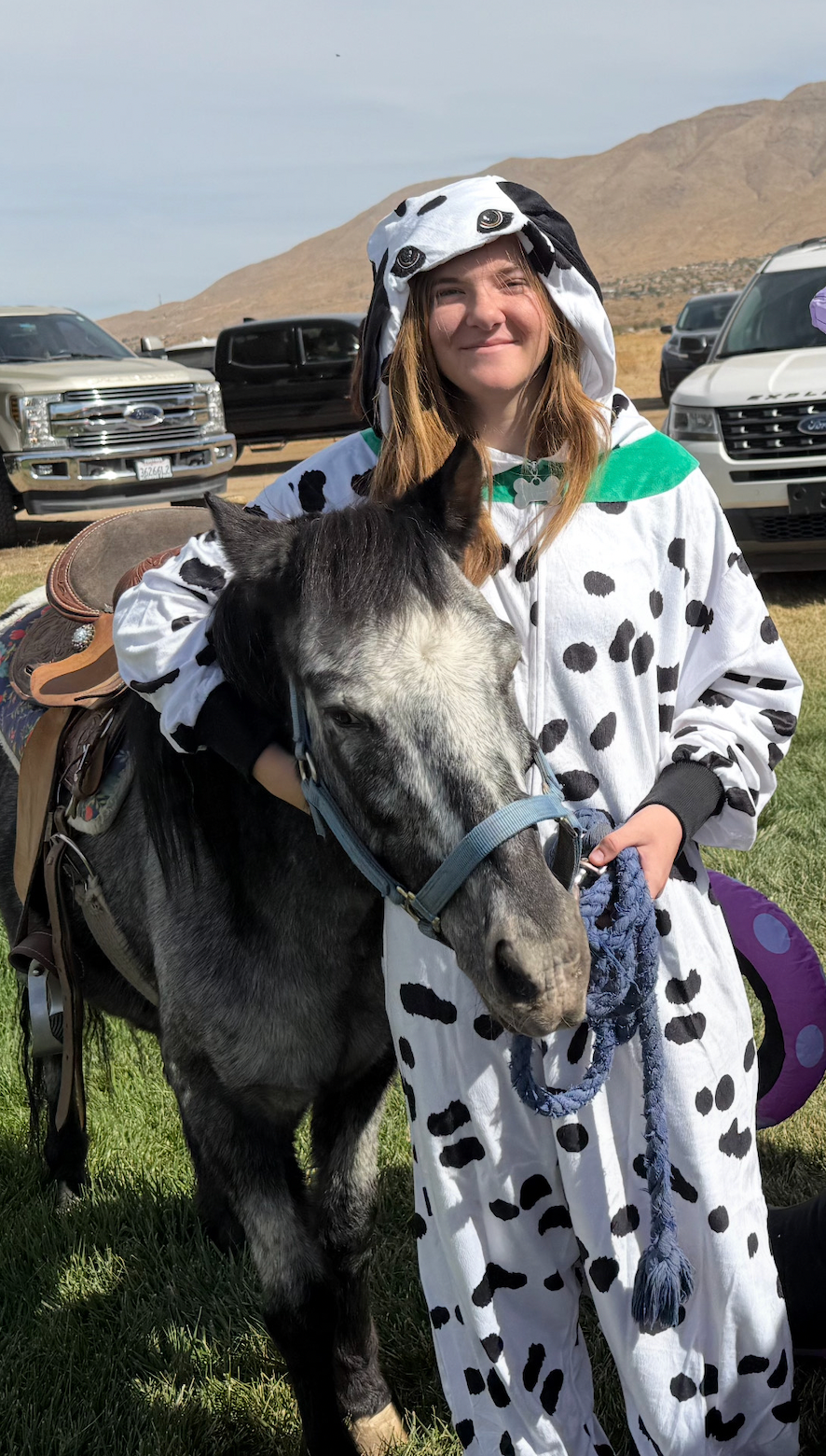 A girl in a dalmatian costume is standing next to a horse.