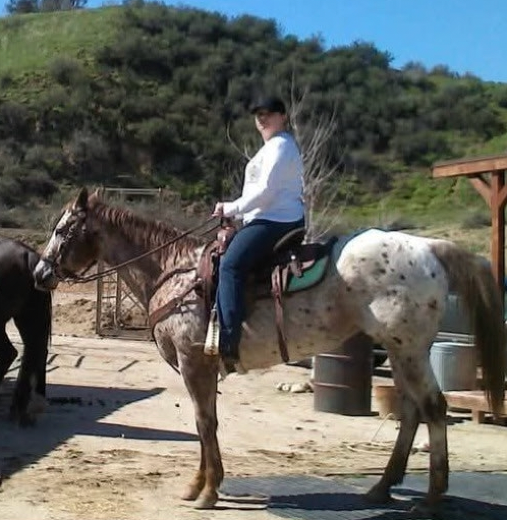 A woman is riding a spotted horse in a dirt field