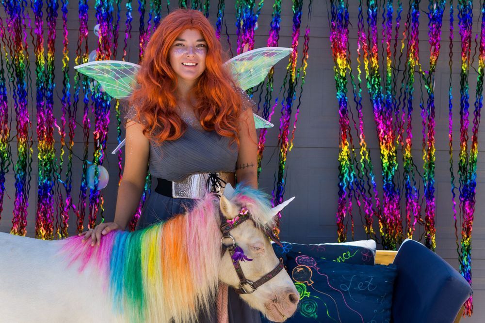 A woman in a fairy costume is standing next to a unicorn.