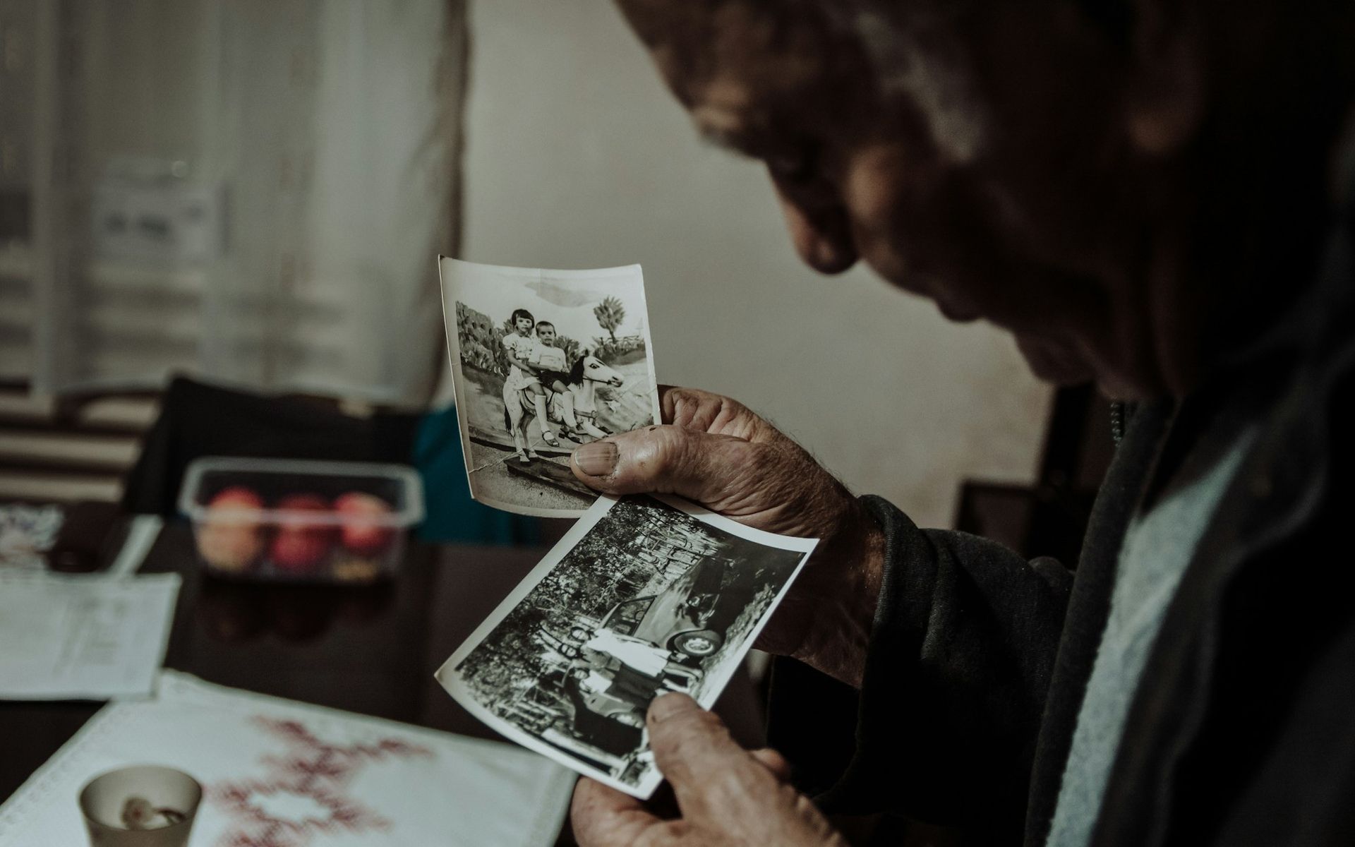 A person's hands hold a framed photograph of a loved one while seated indoors near a wooden table.