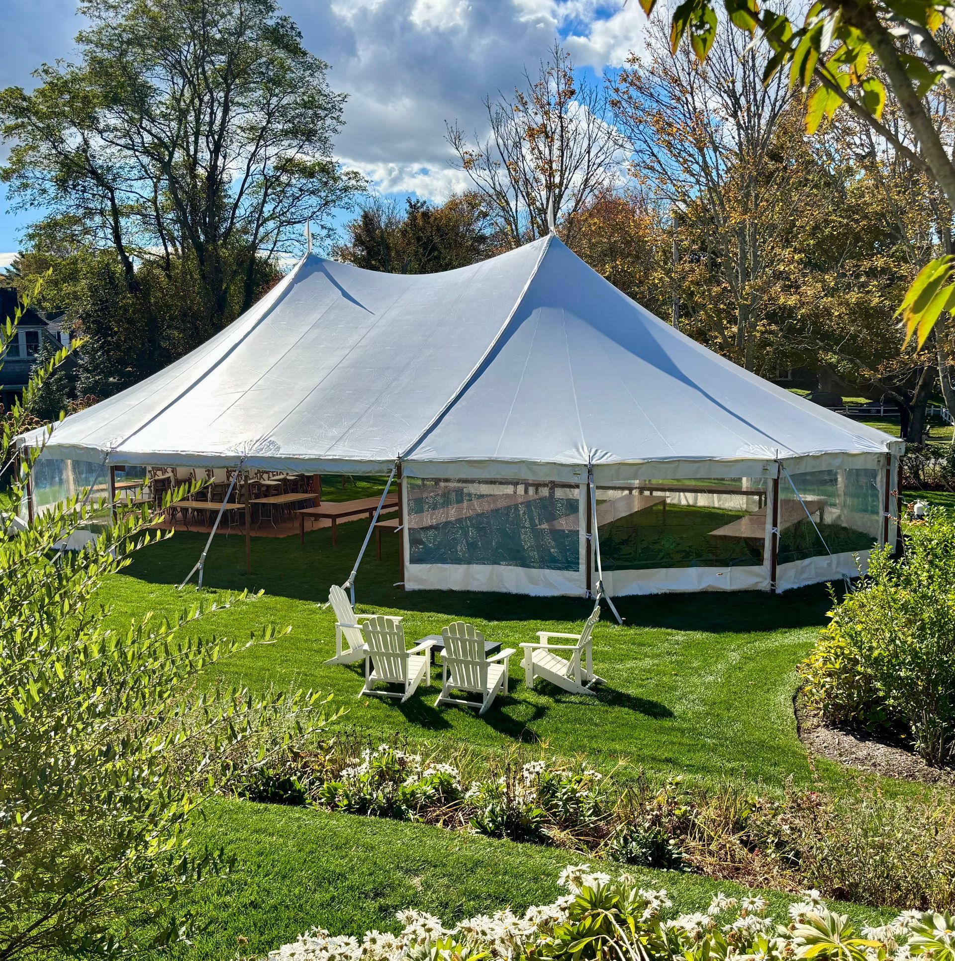 White tent on green grass with clear sides; four white chairs are in front.