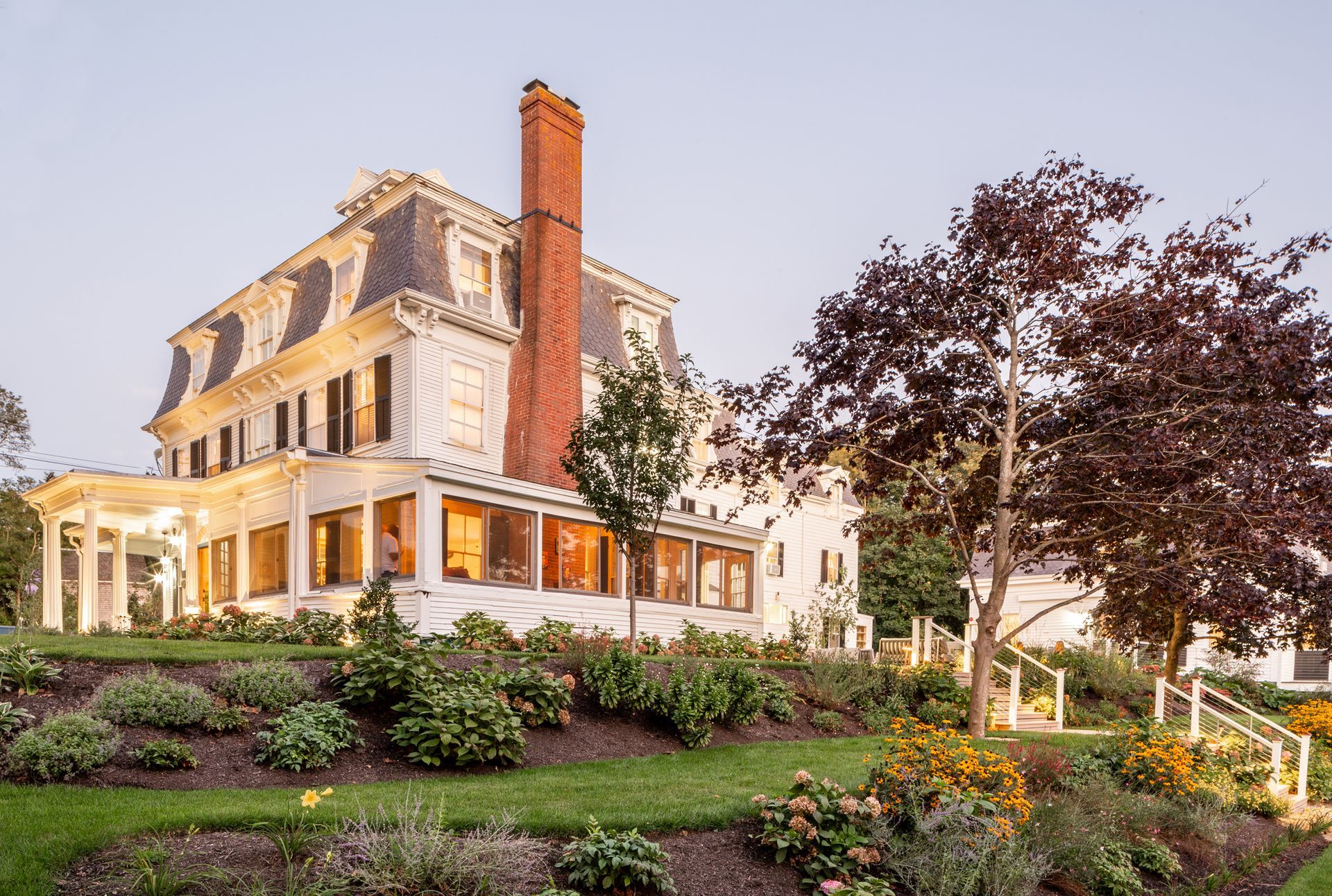 A large white house with a red chimney is sitting on top of a lush green hillside.