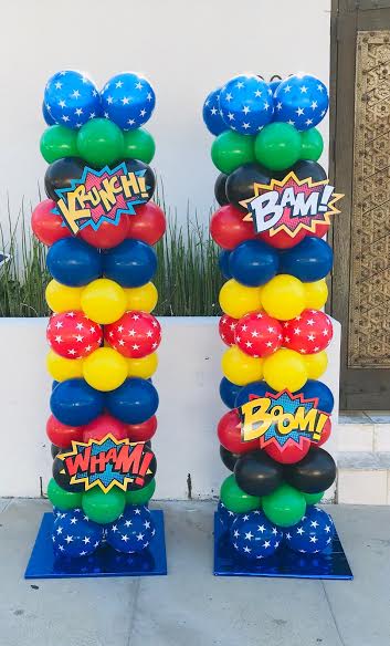 Two superhero-themed balloon columns; blue, green, yellow, red, and black, with comic book sound effects and star balloons.