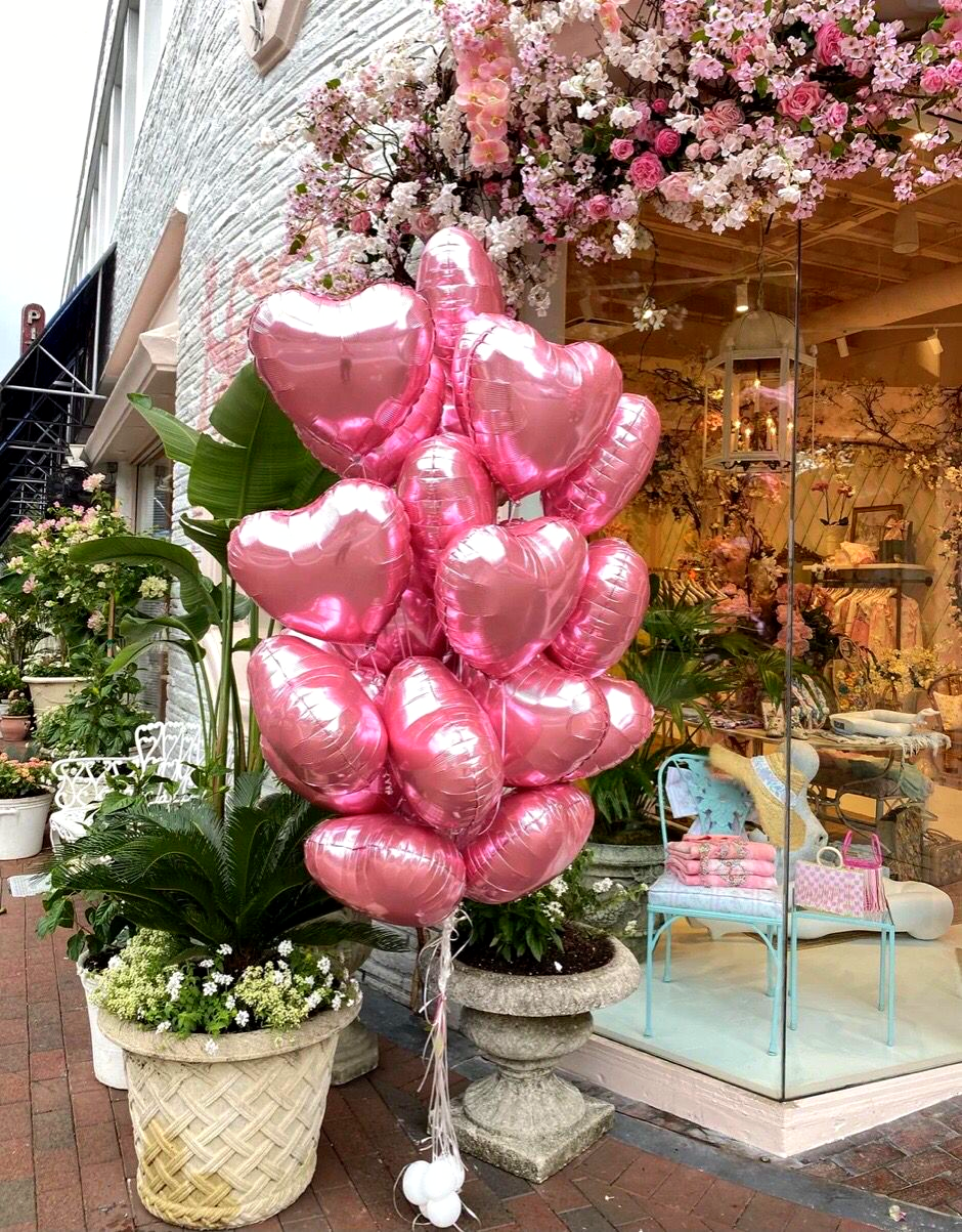 A bouquet of pink heart-shaped balloons outdoors near a flower shop, lush floral decorations.