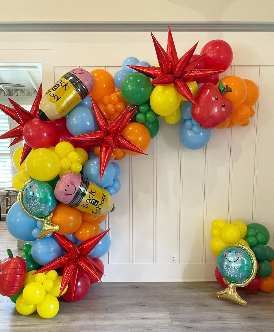 Balloon arch with school-themed elements: pencils, apples, globes, and starbursts, using bright colors.
