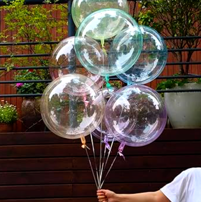A person holding a bouquet of clear, round, inflated balloons with colorful ribbons.