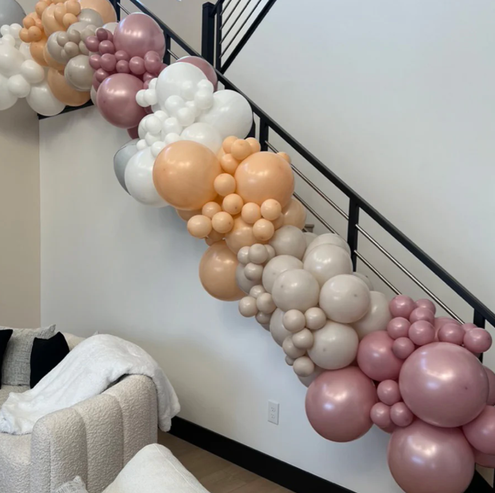 Balloon garland in neutral colors cascading down a staircase with black railing.